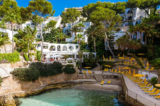 Kleine Bucht mit Steinfelsen auf deinen gelbe Sonnenschirme und Liegen stehen und altes Gebäude zu sehen ist